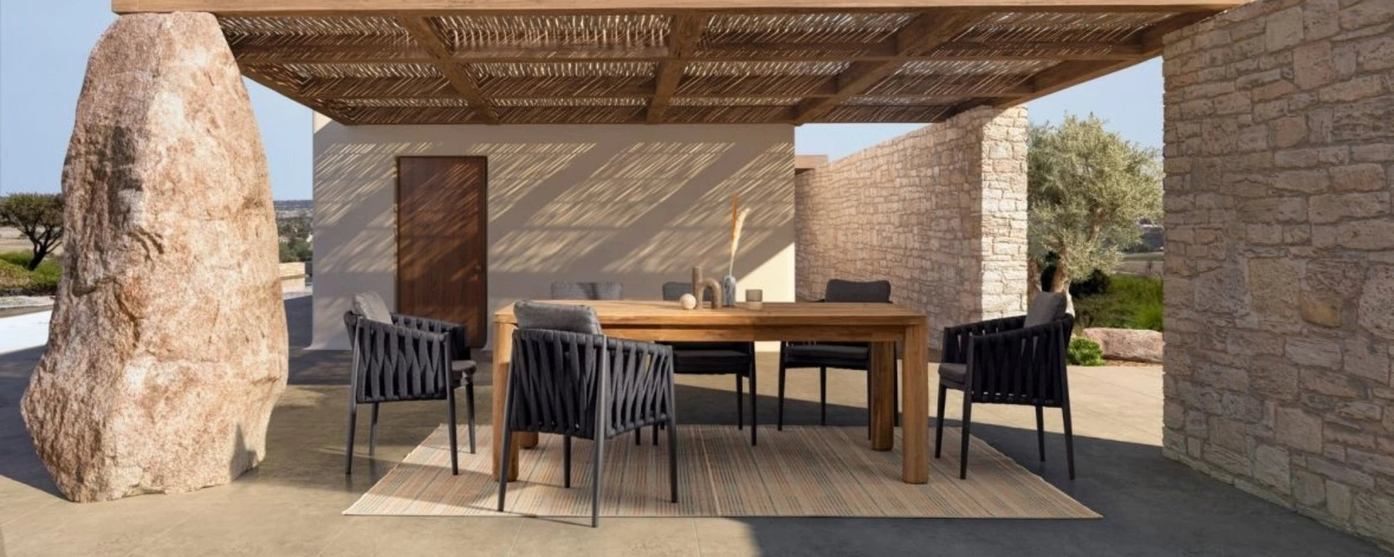 Outdoor dining area with wooden table and chairs under a stone canopy.